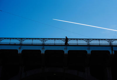 Low angle view of silhouette people on bridge against blue sky