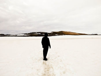 Rear view of man walking on snow covered landscape