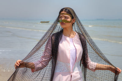 Young woman wearing traditional clothing standing at beach against sky