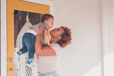 Mom trying to kiss baby boy in front of a yellow door