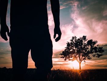 Low section of silhouette man standing by tree against sky during sunset