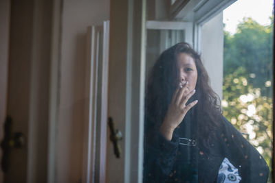 Woman smoking cigarette by window at home