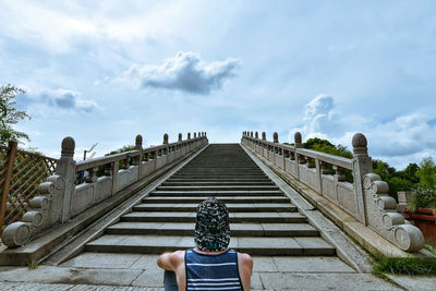 Rear view of man sitting against staircase and sky