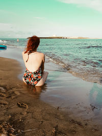 Rear view of woman sitting at beach against sky