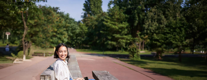 Portrait of smiling young woman standing against trees