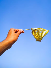 Low angle view of hand holding umbrella against clear blue sky