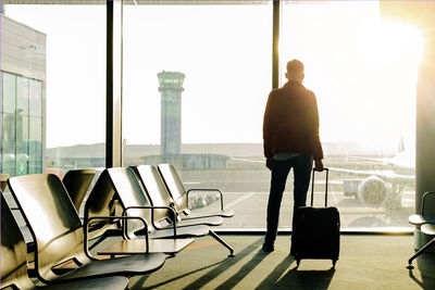 Young tourist with a suitcase standing near the window in airport at early morning sunlight