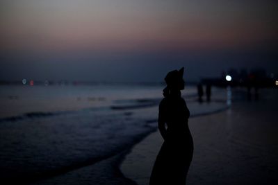 Silhouette woman walking on beach against sky at sunset