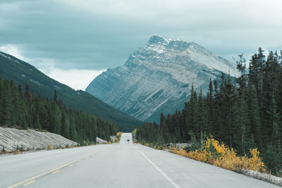 Road amidst trees and mountains against sky