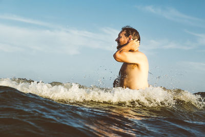 Side view of shirtless man enjoying in sea against sky