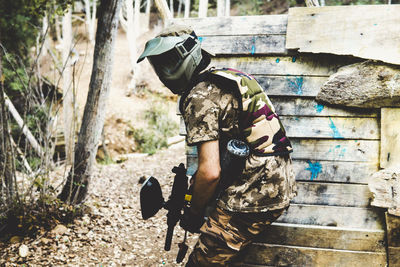 Side view of army solider with gun standing in forest