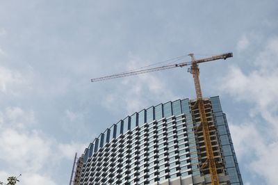 Low angle view of crane by building against sky