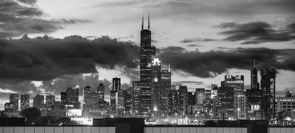 Illuminated buildings in city against cloudy sky