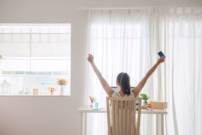 Woman with arms raised while standing on table at home