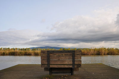 Empty bench by lake against sky