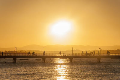 Silhouette bridge over sea against sky during sunset