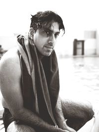 Shirtless wet mid adult man with towel looking away while sitting at poolside