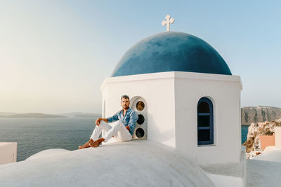Man sitting by chapel against sea