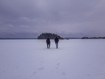 People walking on snow covered landscape against sky