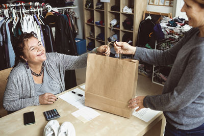 Happy cashier giving shopping bag to customer in clothing store