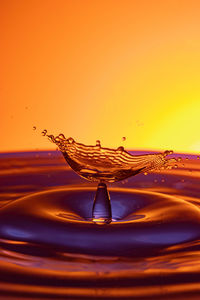 Close-up of drop falling on water against orange background