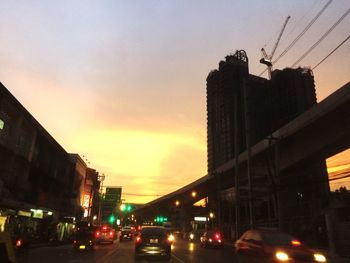 Cars on road in city against sky during sunset