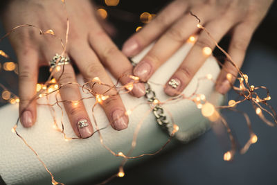 Cropped hands with illuminated string lights and purse on table