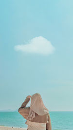 Rear view of woman standing at beach against sky