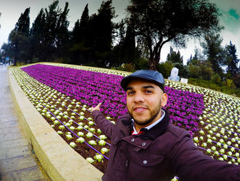 Portrait of young man standing against purple flowering plants