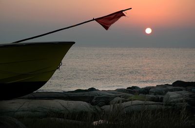 Boat with flag on shore overlooking sea during sunset