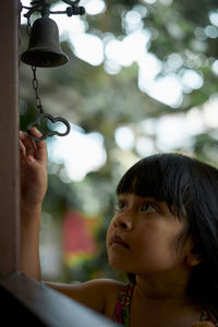 Close-up of girl holding bell seen through door