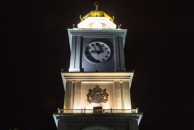 Low angle view of clock tower against illuminated building at night