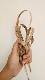 Cropped hand of woman holding tape measure against white background