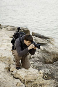 Photographer takes picture of something while kneeling on rock by sea. man travels around malta.