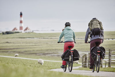 Rear view of people riding bicycle on field