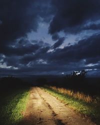 Illuminated dirt road amidst agricultural field against cloudy sky