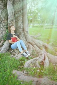 Woman with book leaning on tree at park