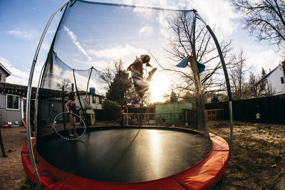 Girl jumping while sister standing in trampoline at backyard