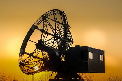 Low angle view of silhouette ferris wheel against orange sky