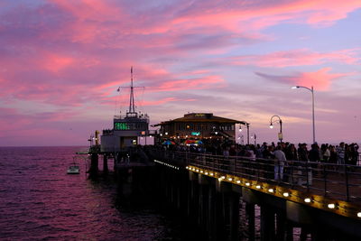 Illuminated pier over sea against sky at sunset