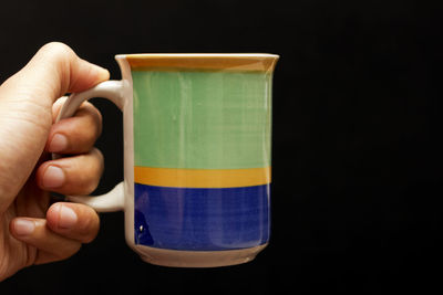 Cropped hand holding cup against black background