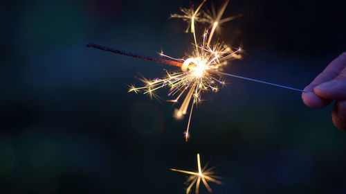 Cropped hand with burning sparkler at night