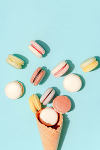 French dessert concept, colorful pastel macarons are served in waffle cone on light blue background.