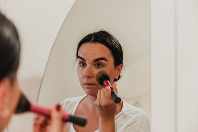 Mirror photo of beautiful young woman putting on make-up