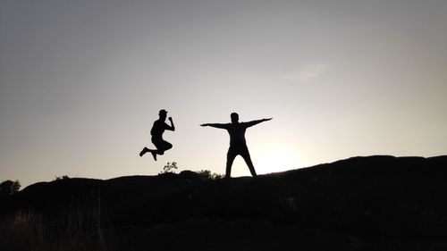 Silhouette people with arms outstretched standing against sky during sunset