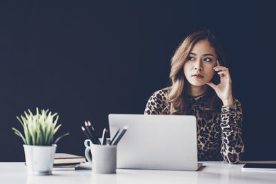 Thoughtful businesswoman sitting at desk against black background