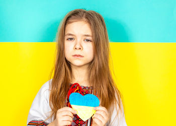 A girl in an embroidered shirt holds a heart painted in yellow and blue as a sign of love for ukrain