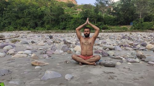 Full length of shirtless man on rock against trees