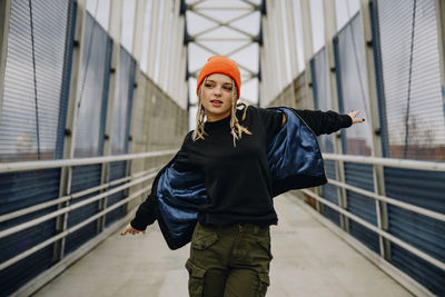 Beautiful woman wearing jacket with arms outstretched dancing on footbridge