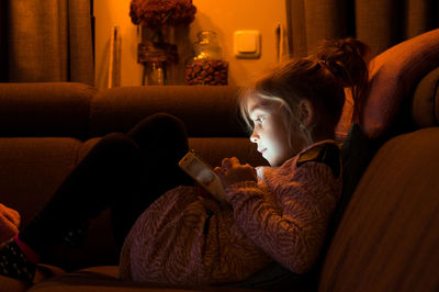 Side view of girl using mobile phone while sitting on sofa at home